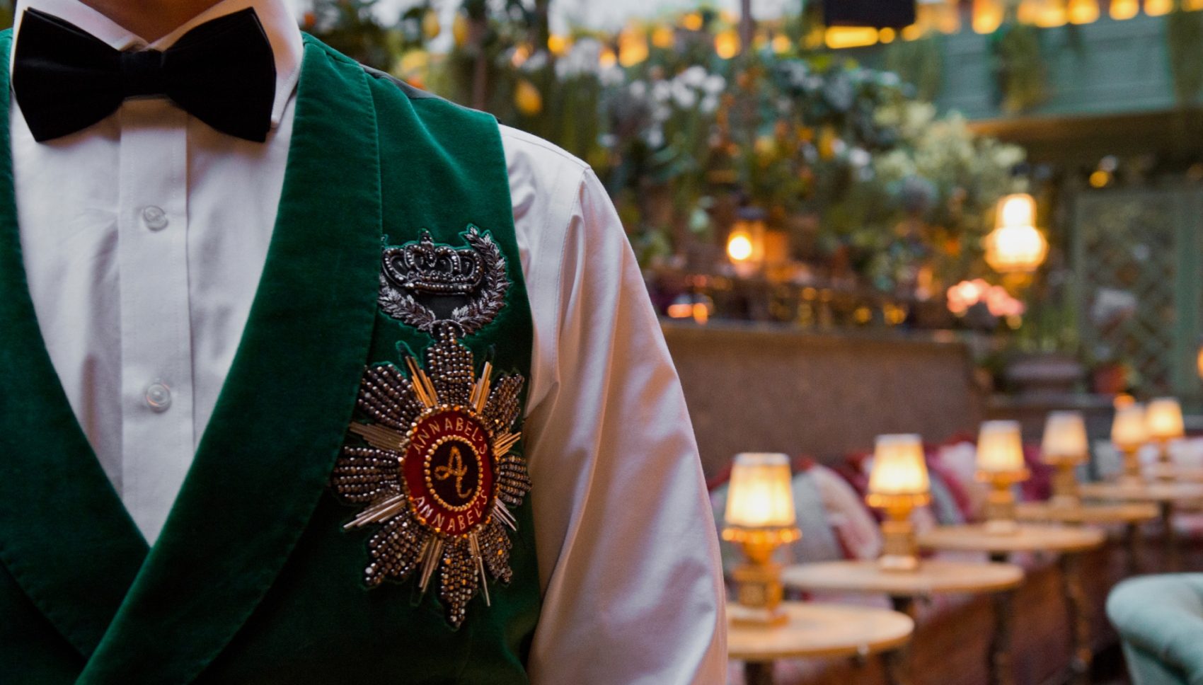 Waiter in a green velvet jacket with an embroidered crest