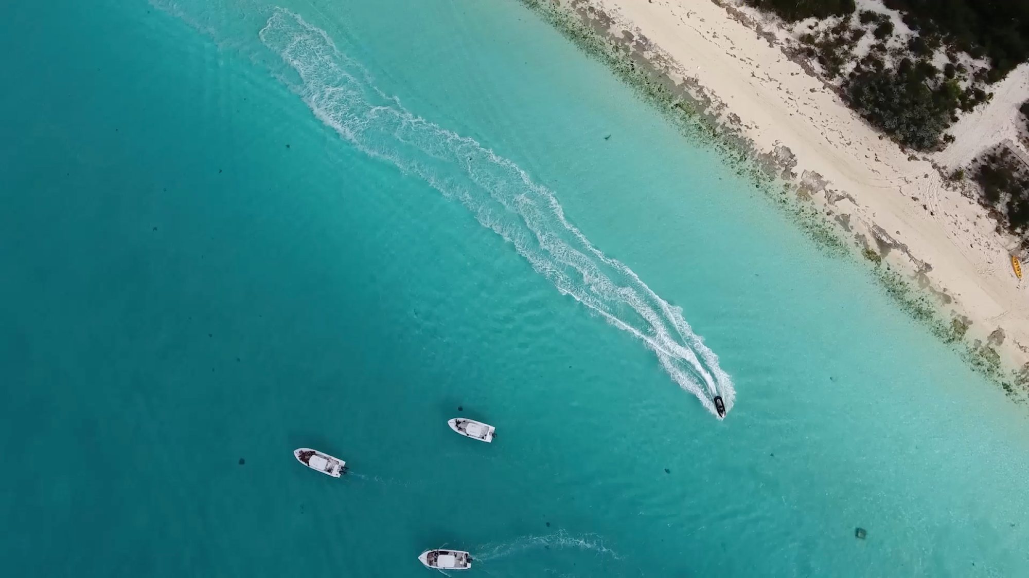Aerial shot of speedboats crossing turquoise shallows off a white-sand beach